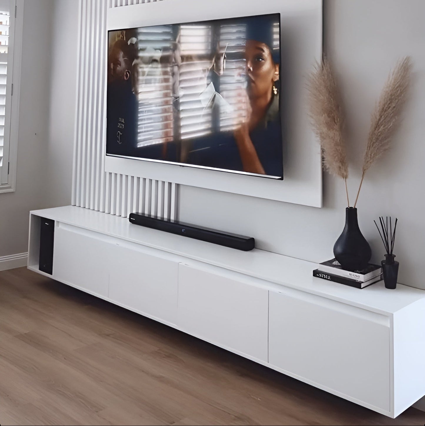 Modern living room with a television mounted on the wall, soundbar below, and decorative items on a white console.