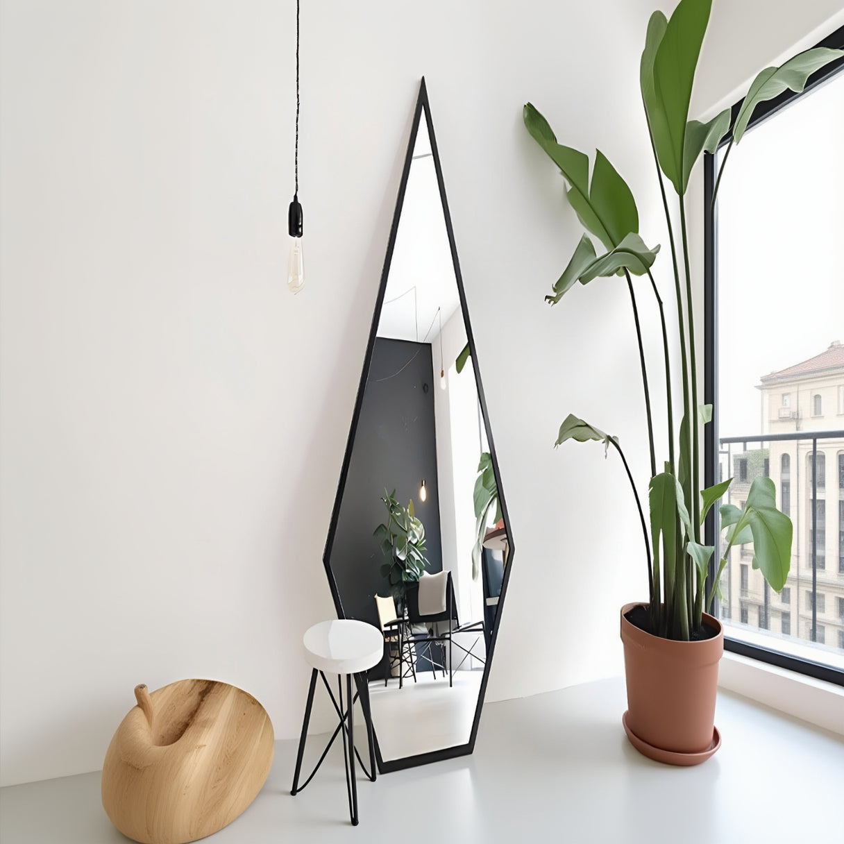 Tall black-framed mirror leaning against a white wall with a plant to the right.