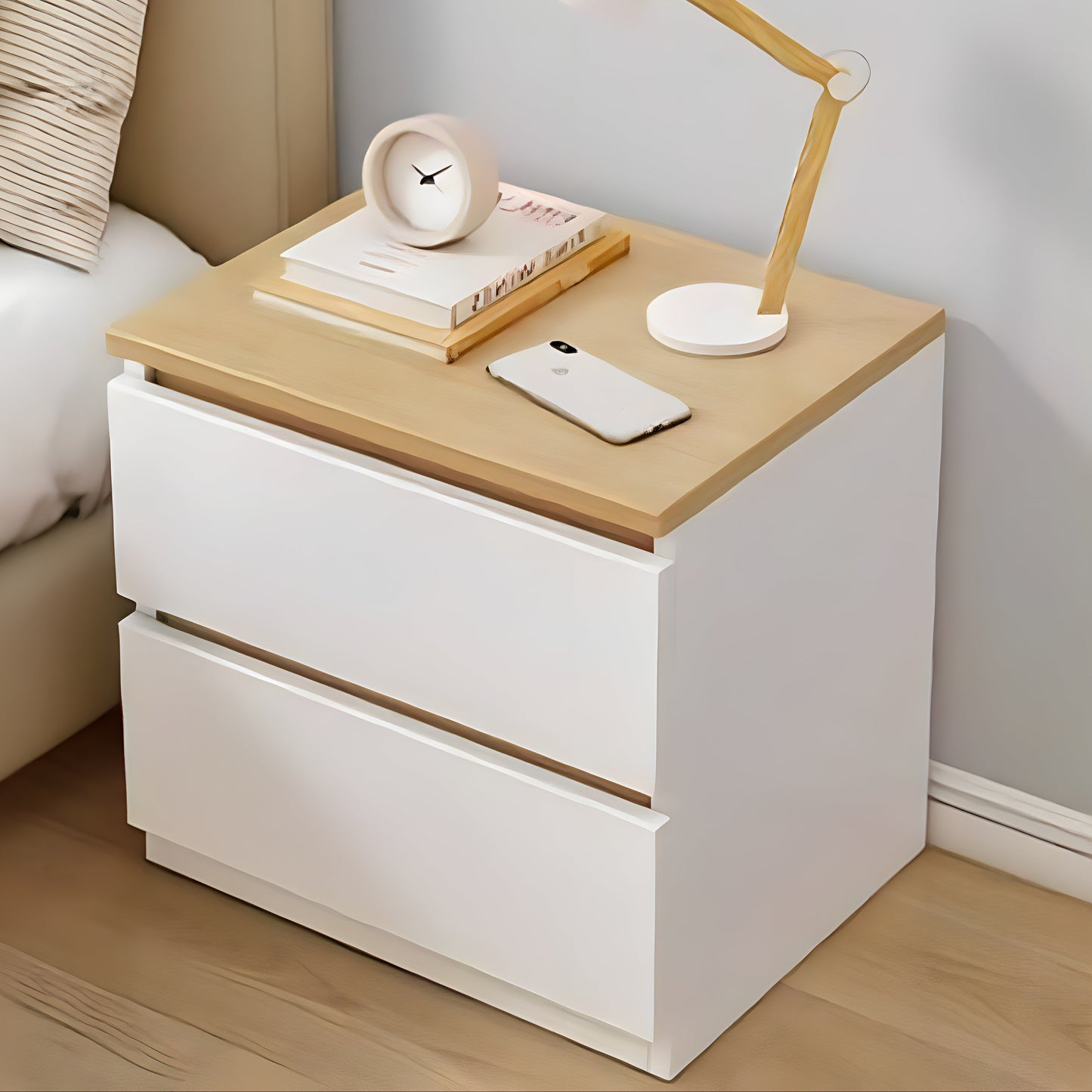 White nightstand with wooden top featuring a lamp, phone, and books in a bedroom setting.