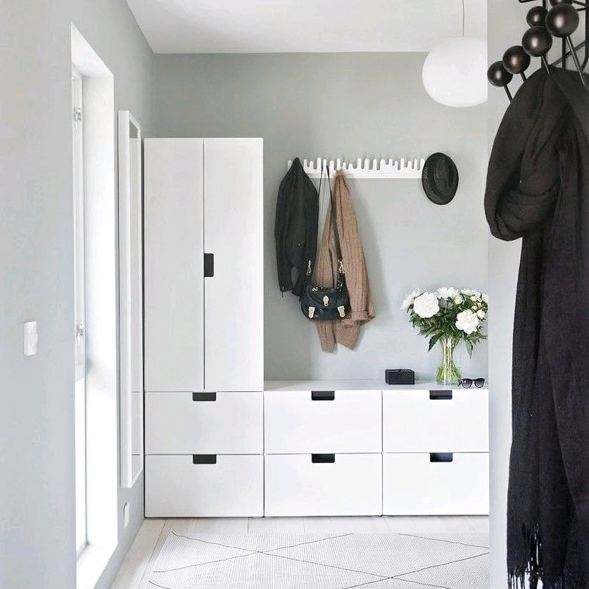 Modern hallway with white cabinets, black-framed mirrors, and a coat rack with hanging coats.