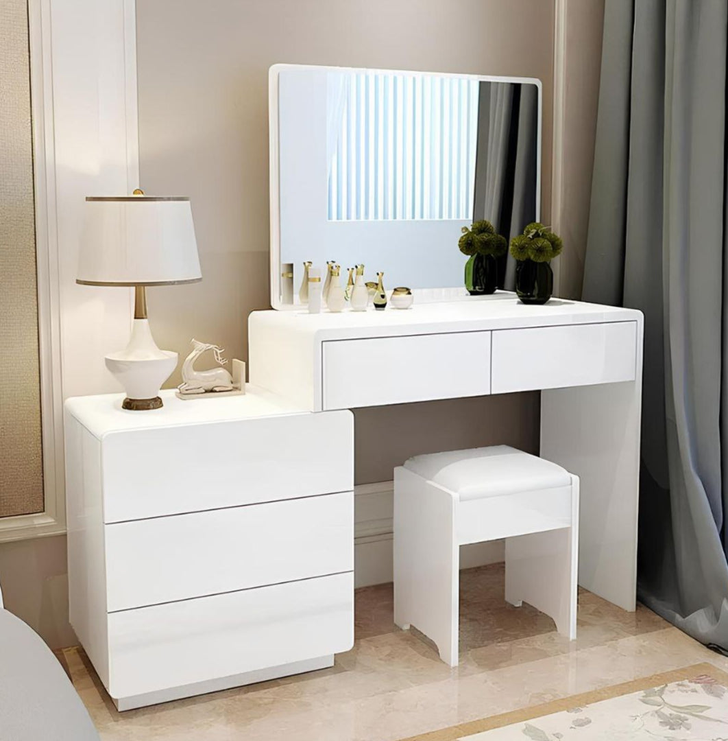 White vanity table with mirror, lamp, and stool in a room setting.