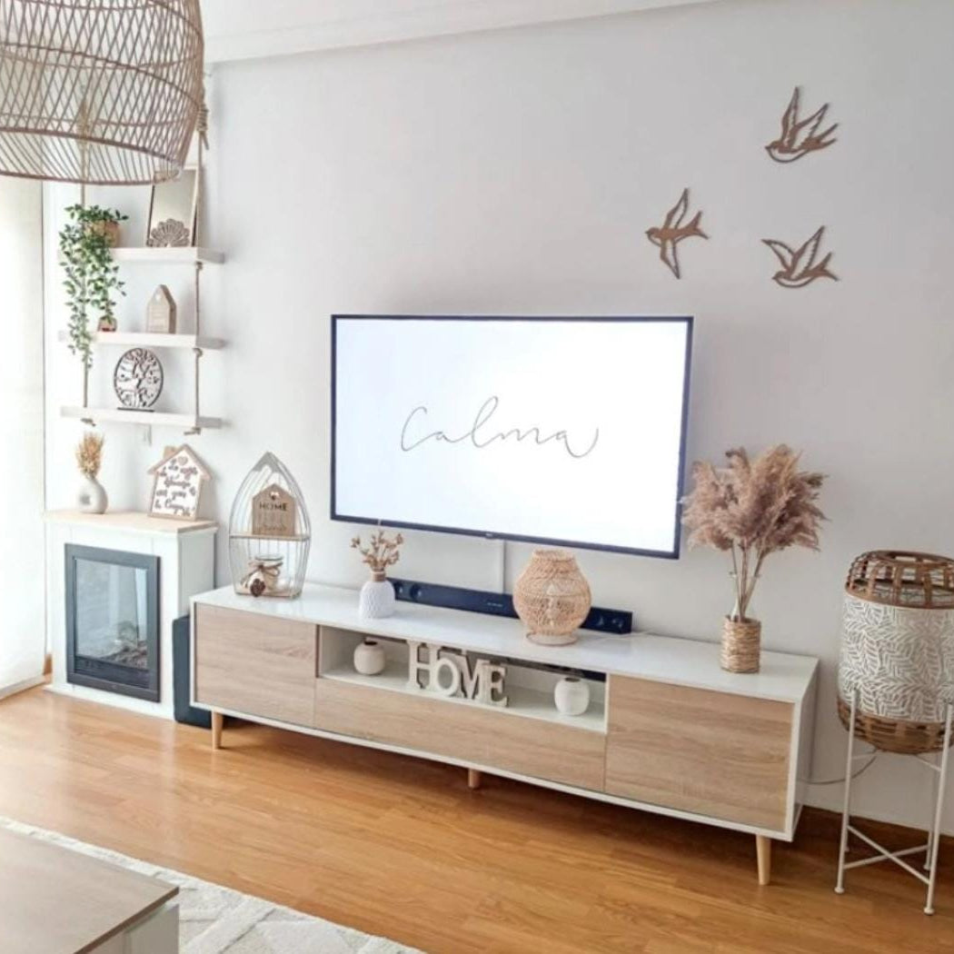 A modern living room setup featuring a light wood and white TV console with a mounted flat-screen television. The room has light wood floors, a white wall decorated with three bird silhouettes, and a large woven pendant light hanging on the left.
