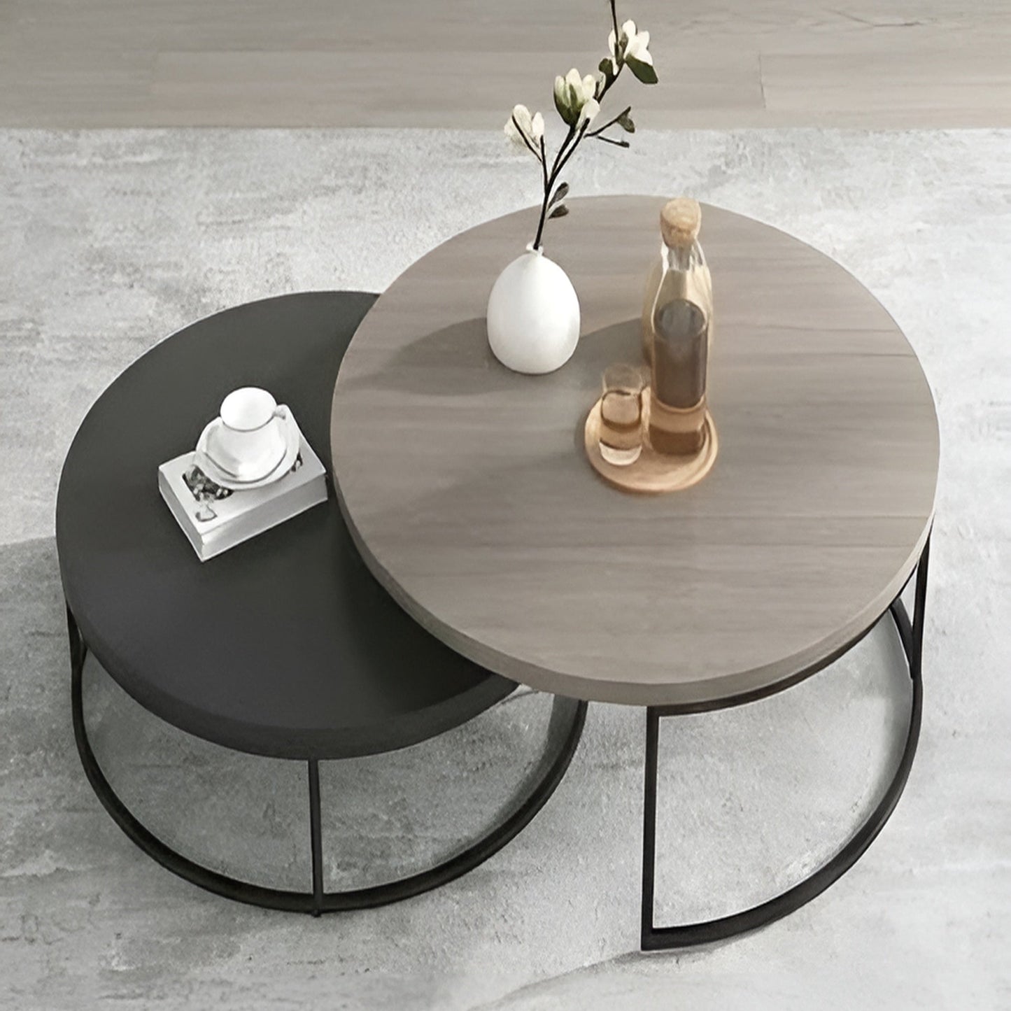 Two round coffee tables, one black and one gray with decorative items on a light gray floor.