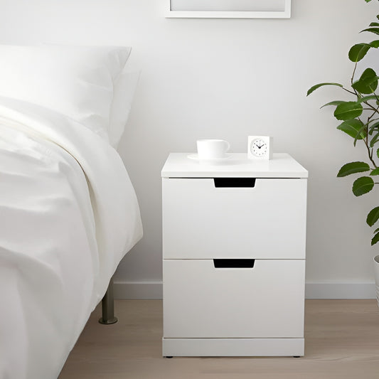 White nightstand with a drawer next to a bed in a bedroom setting.