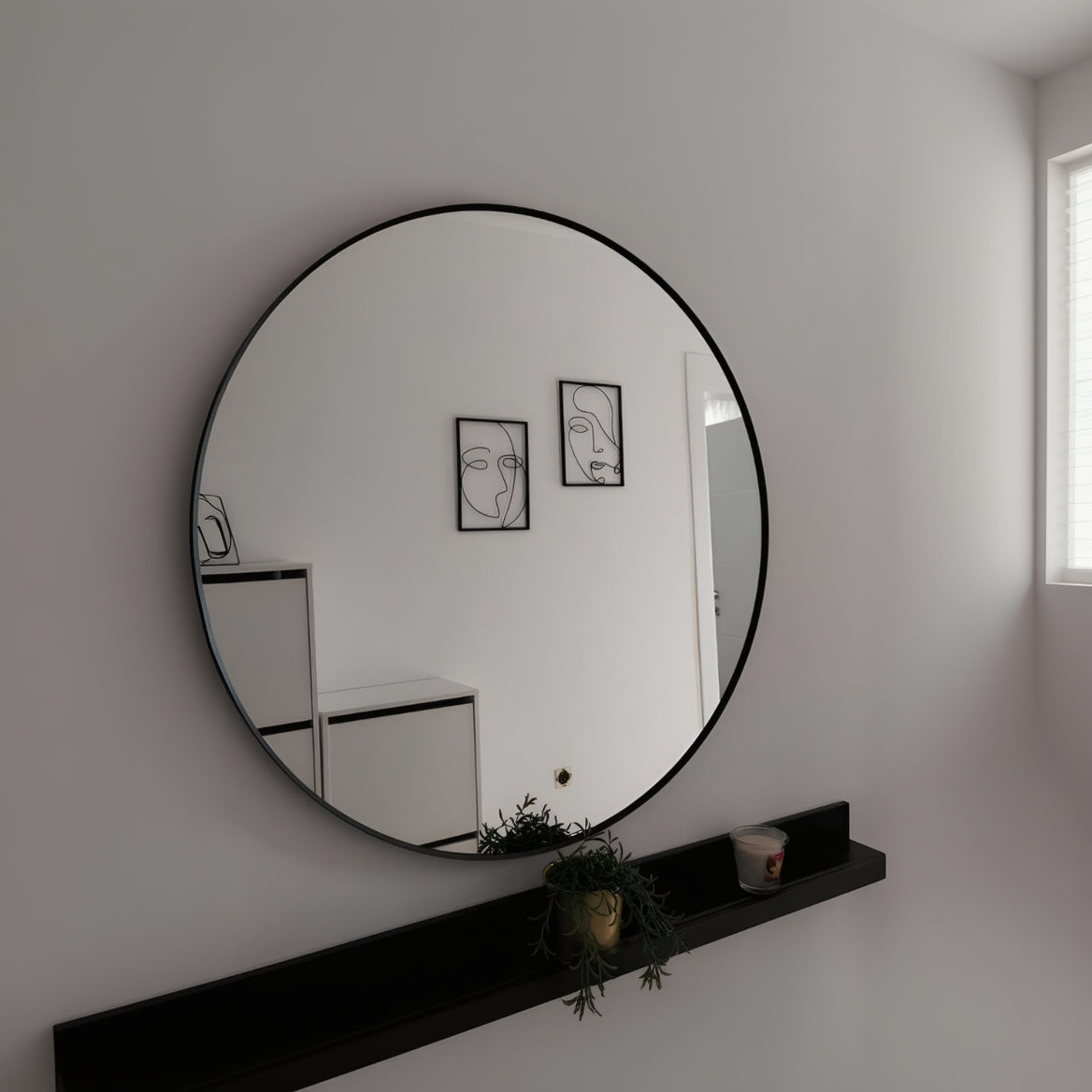 Round mirror with black frame on a white wall with minimal decor.