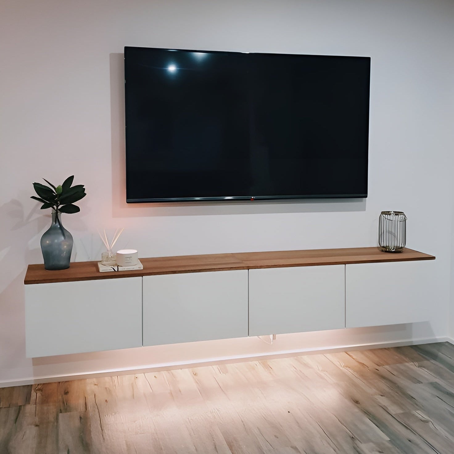 Modern living room with a large flat-screen TV mounted on the wall above a wooden shelf.