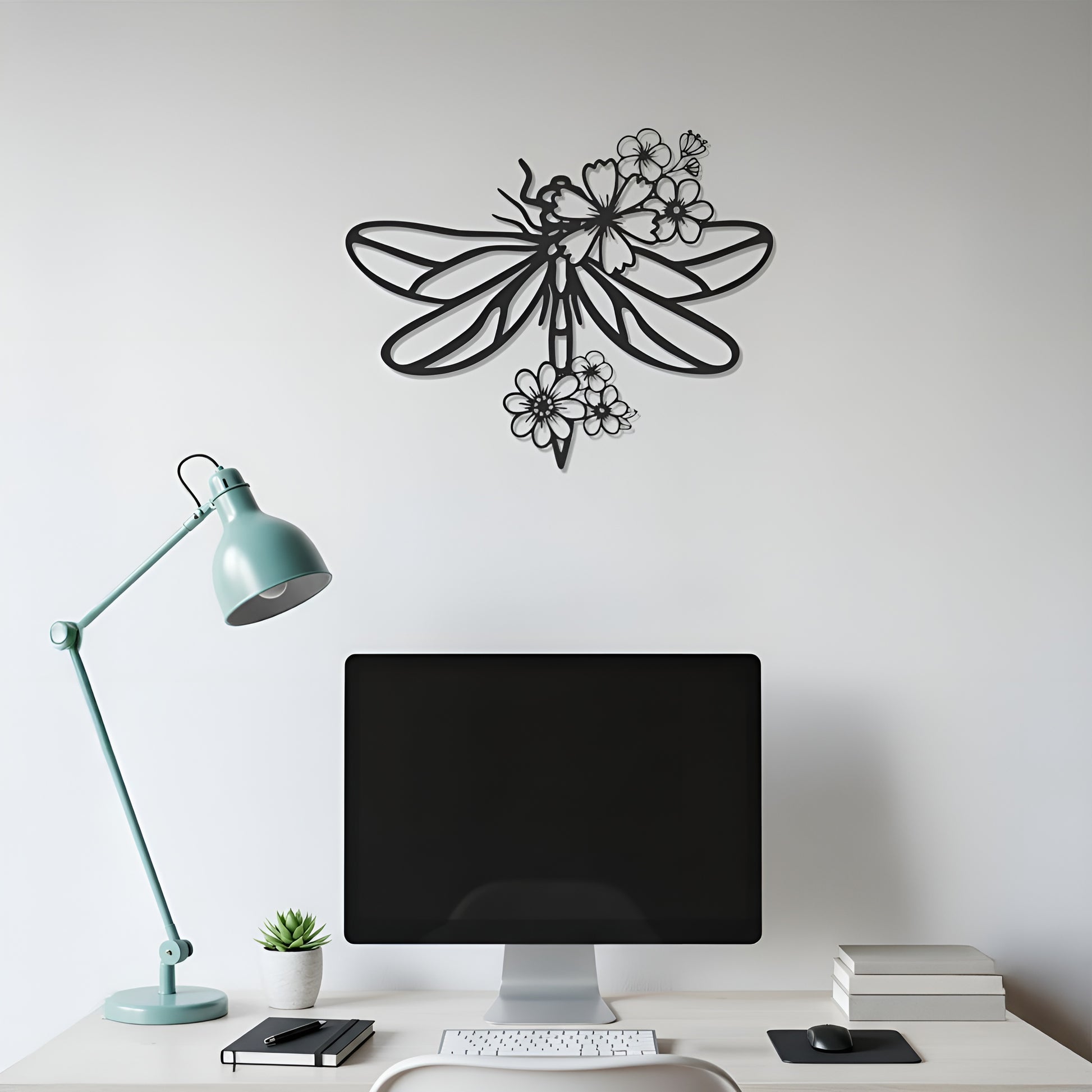 Decorative metal wall art of a dragonfly on a white wall above a desk with a computer monitor.