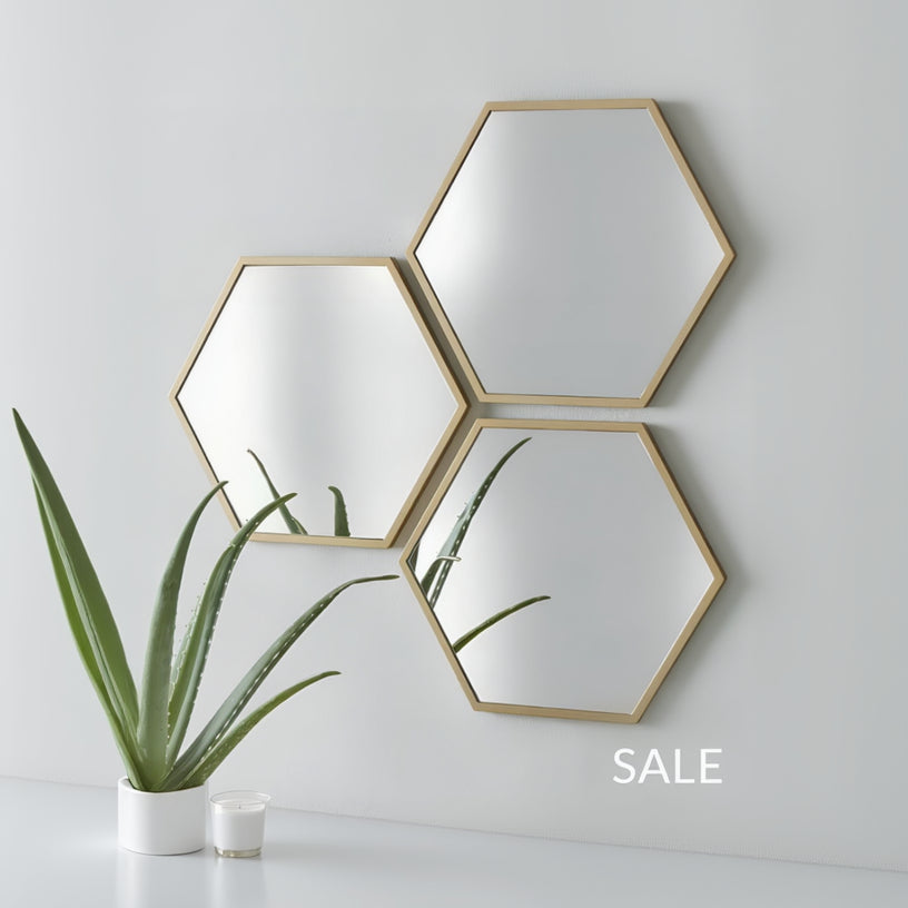 Three hexagonal mirrors with gold frames on a white wall, with a plant and books in the foreground.