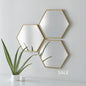Three hexagonal mirrors with gold frames on a white wall, with a plant and books in the foreground.
