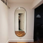 Oval mirror on a white wall reflecting a room with wooden floor.