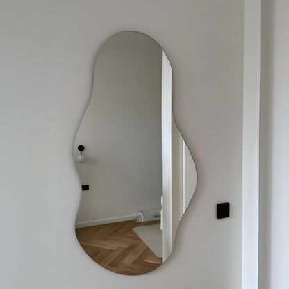 Wavy mirror on a white wall reflecting a room with wooden flooring.