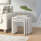 Set of white nesting tables with a plant and candle on top, next to a white sofa.