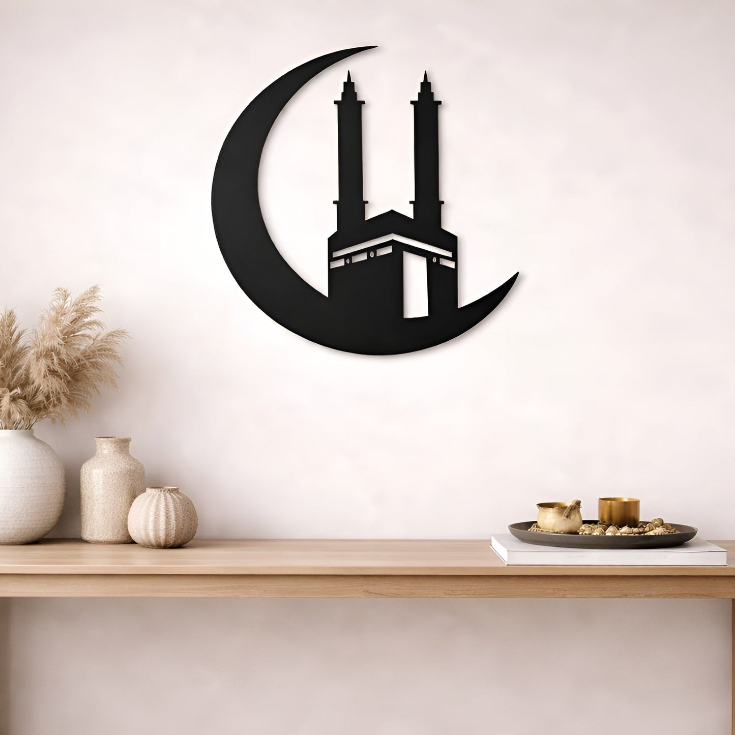 Decorative wall art of a crescent moon with a building silhouette on a white wall above a wooden table.