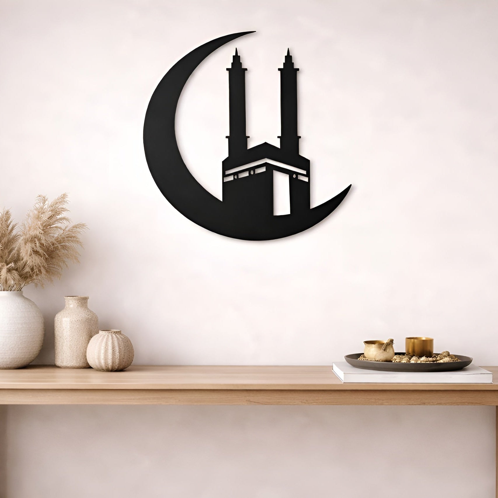 Decorative wall art of a crescent moon with a building silhouette on a white wall above a wooden table.