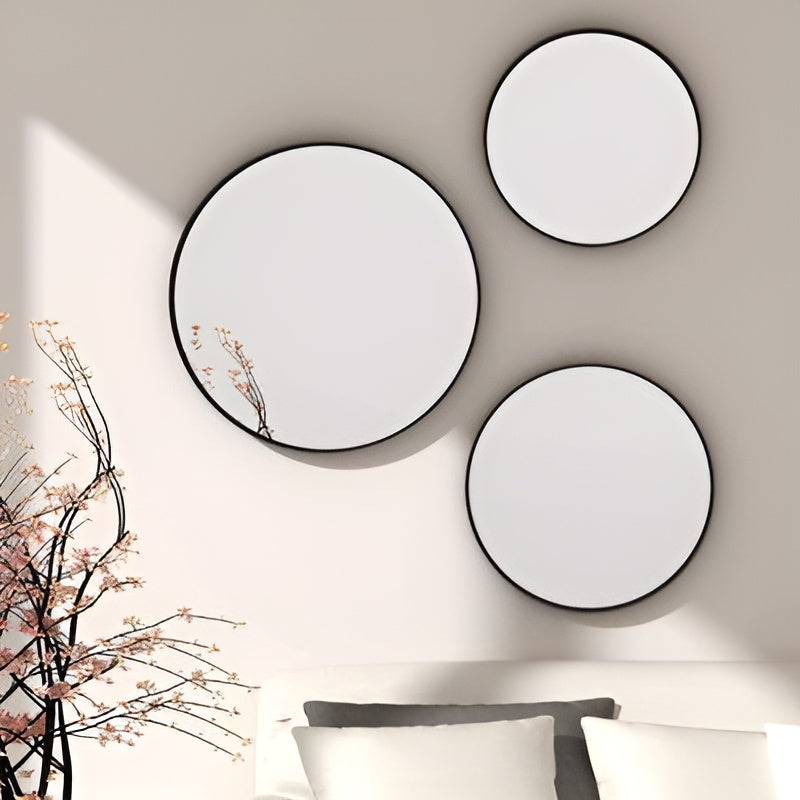 Three round wall mirrors with black frames on a beige wall.
