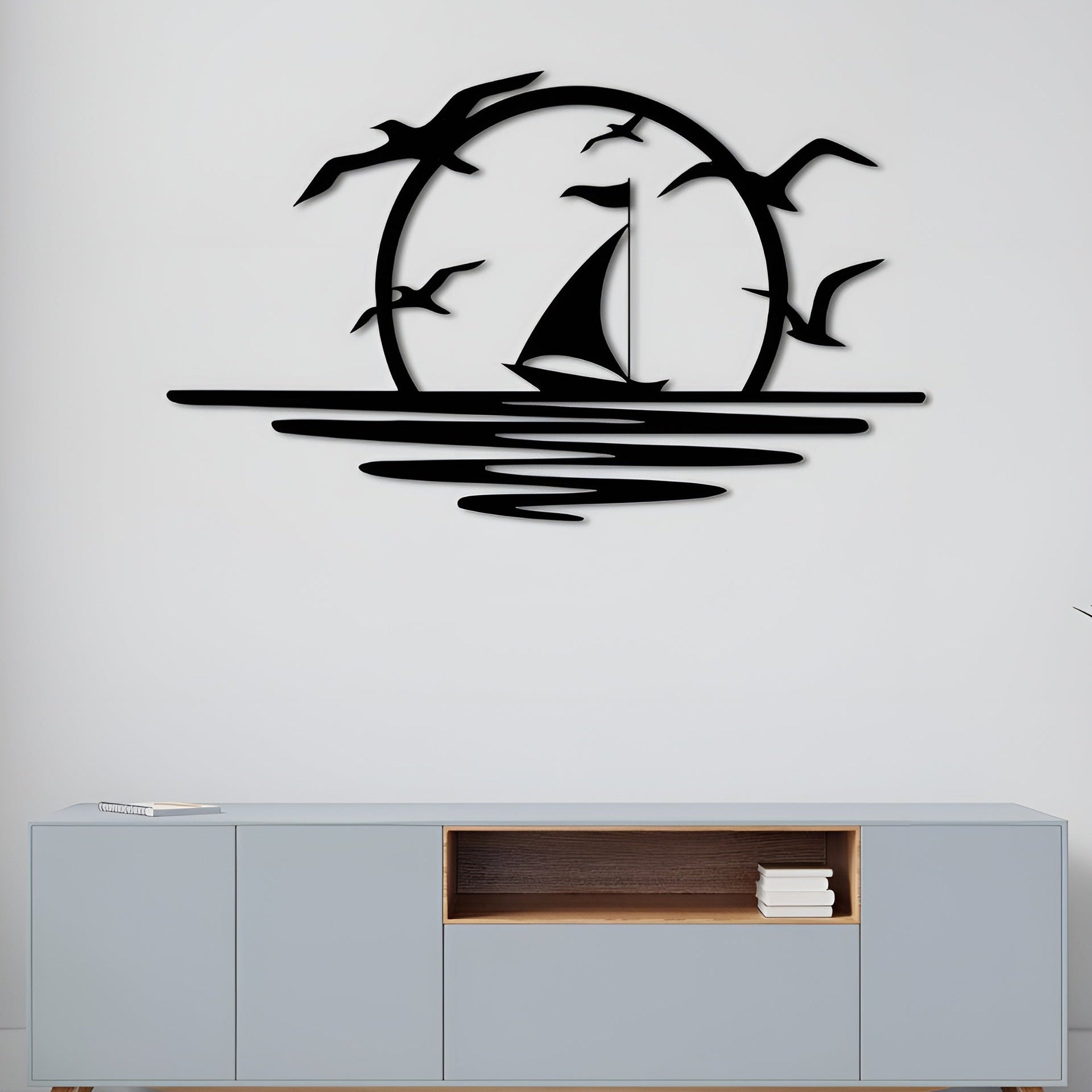Decorative wall art of a sailboat and birds on a white wall above a light gray cabinet.