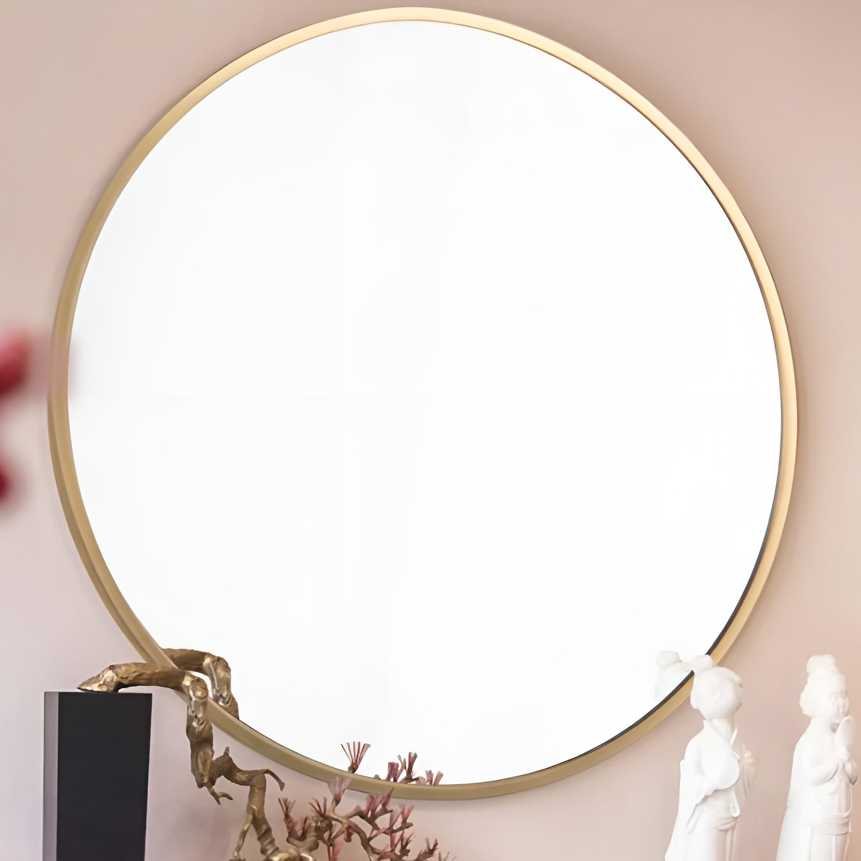 Round mirror with gold frame on a beige wall, featuring decorative elements.