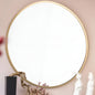 Round mirror with gold frame on a beige wall, featuring decorative elements.
