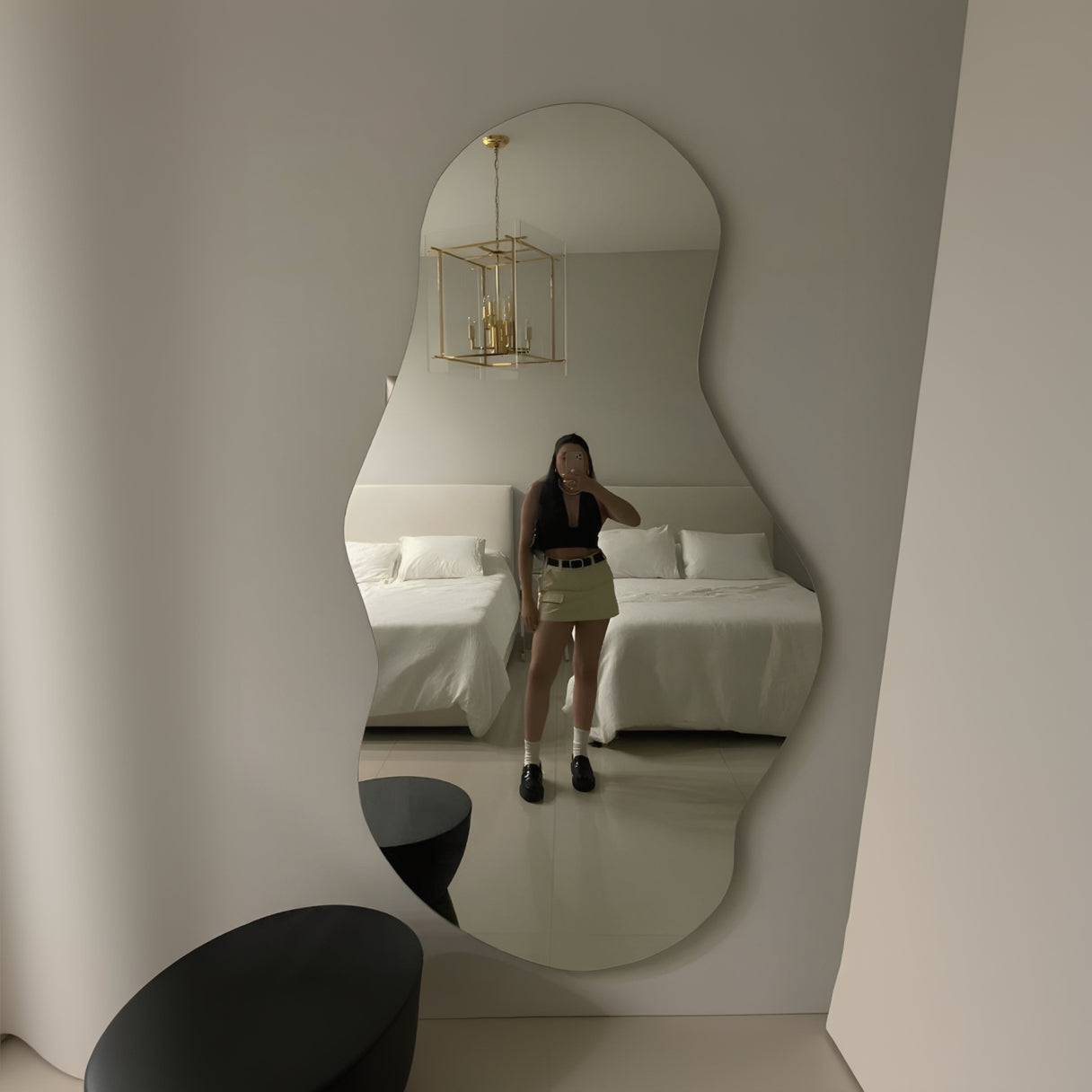 Person taking a mirror selfie in a bedroom with a bed and lamp.