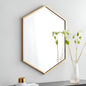 Hexagonal gold-framed wall art on a light gray wall with a vase of plants on a surface.