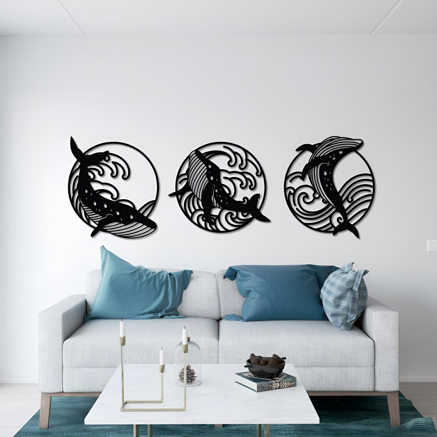 Three black dolphin wall decorations on a white wall above a white sofa with blue pillows.