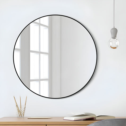 Round mirror with black frame on a white wall above a wooden desk.