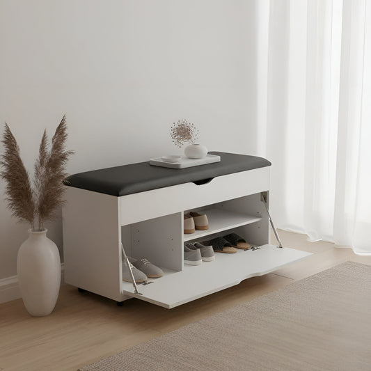 White shoe storage bench with black top in a room with light wood flooring and white curtains.