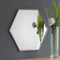 Hexagonal mirror on a gray wall with a side table and flowers in the foreground