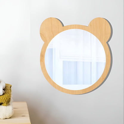 Wooden children's mirror with bear ears on a white wall above a wooden shelf with toys.
