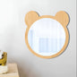 Wooden children's mirror with bear ears on a white wall above a wooden shelf with toys.