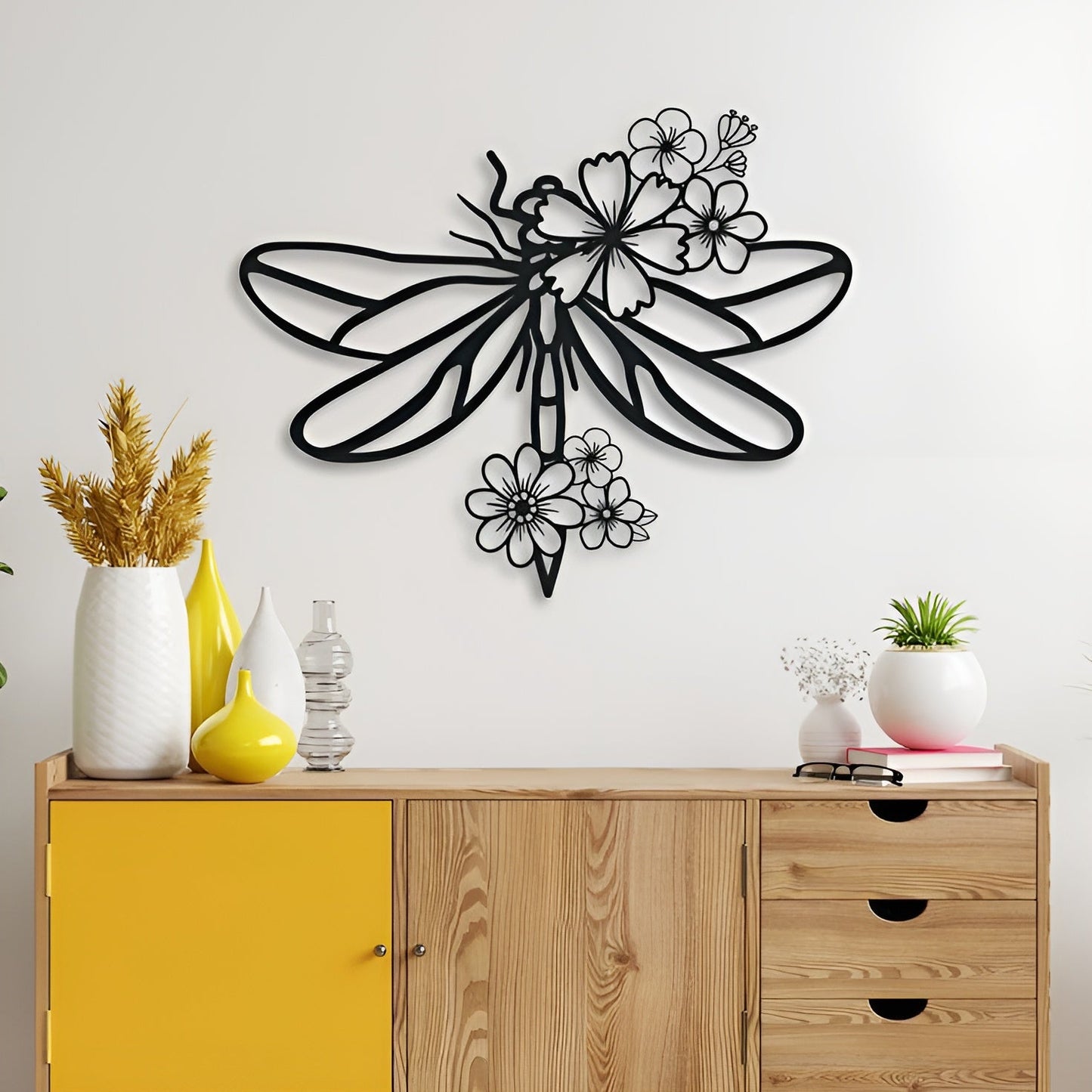 Decorative wall art of a dragonfly on a white wall above a wooden cabinet with yellow door.