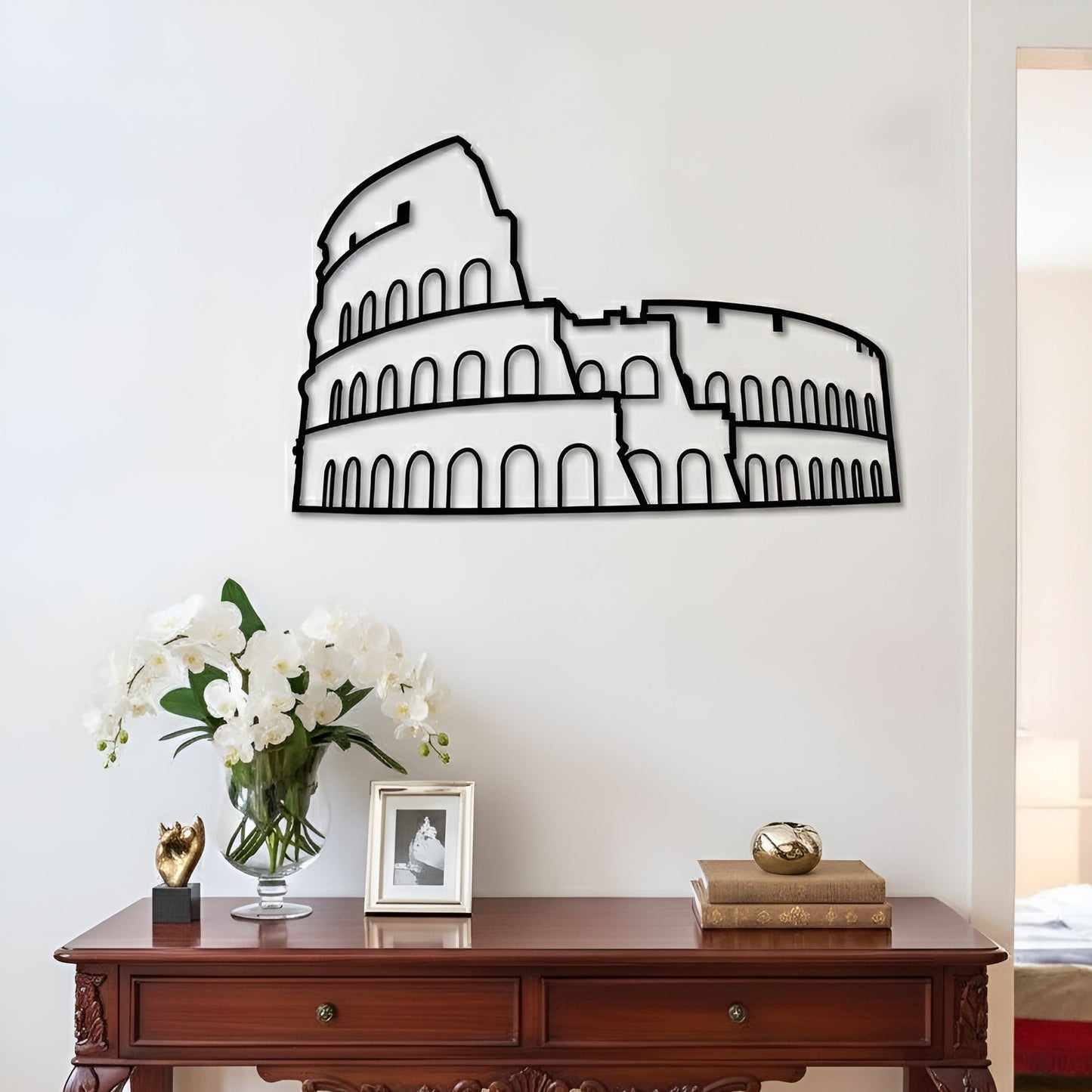 Decorative wall art of the Colosseum on a white wall above a wooden console table with decor items.