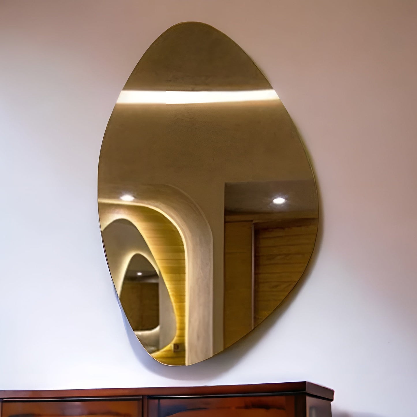 Gold oval mirror on a white wall with a wooden cabinet below