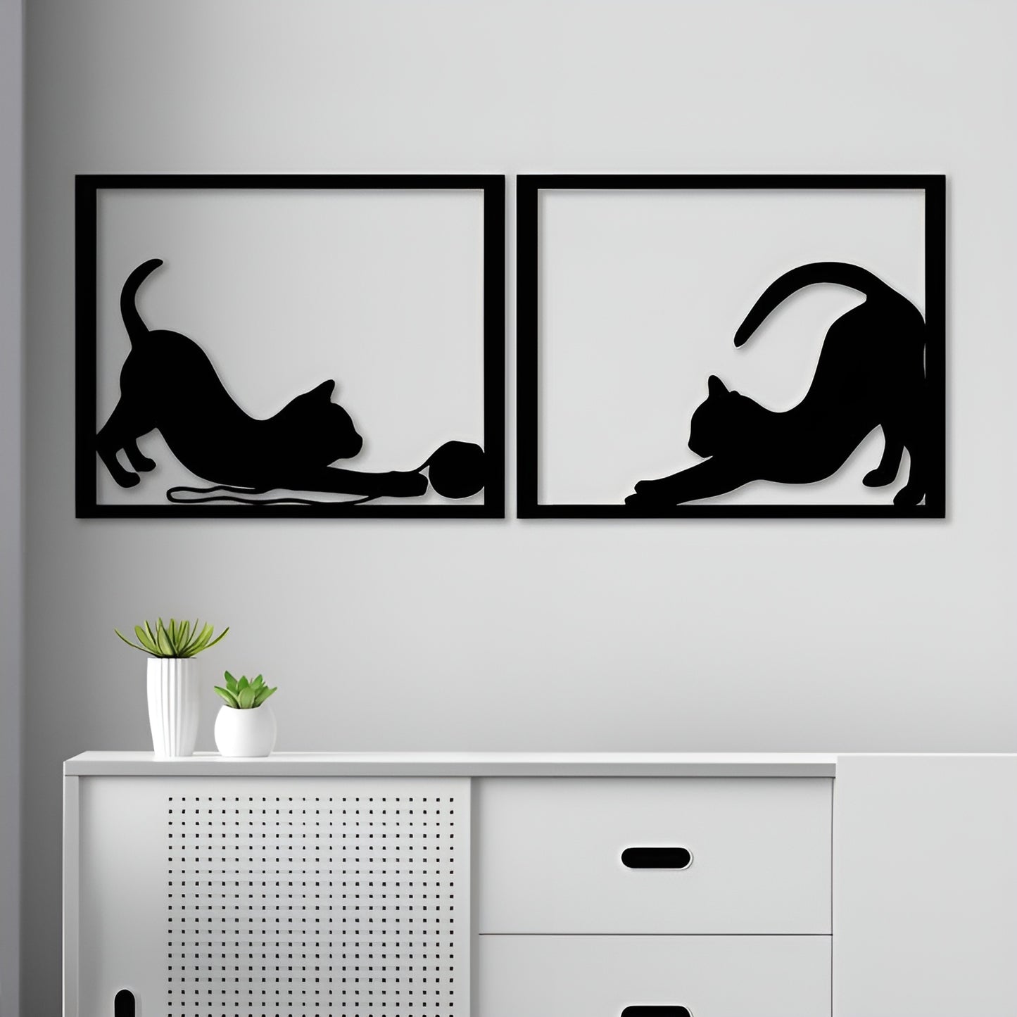 Two black framed wall art pieces of cats on a gray wall above a white cabinet.