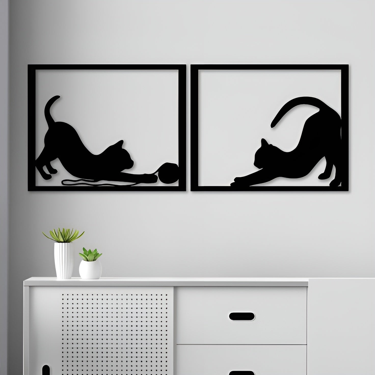 Two black framed wall art pieces of cats on a gray wall above a white cabinet.