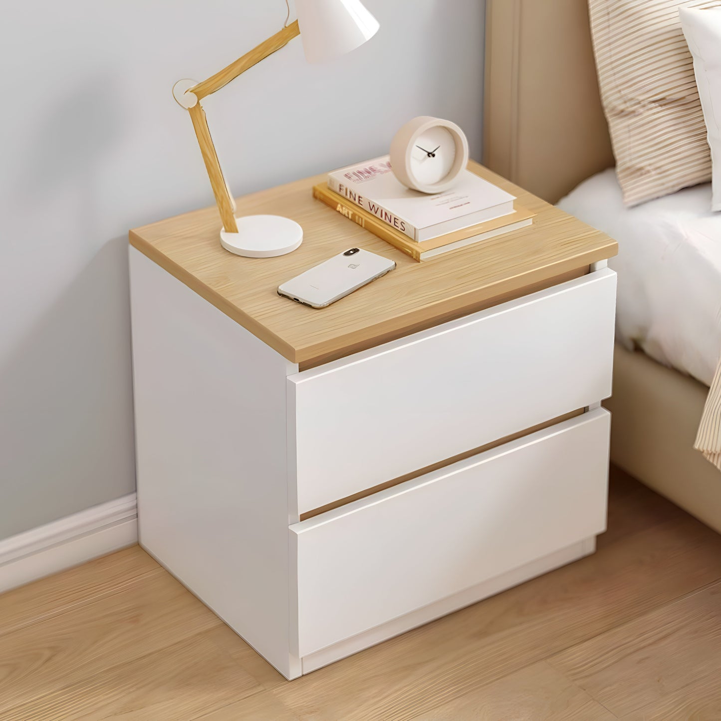 White nightstand with wooden top next to a bed, featuring a lamp, books, and phone.
