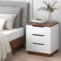 White nightstand with wooden top next to a bed in a bedroom.