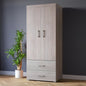 Wooden wardrobe with two doors and two drawers against a dark wall with a plant beside it.