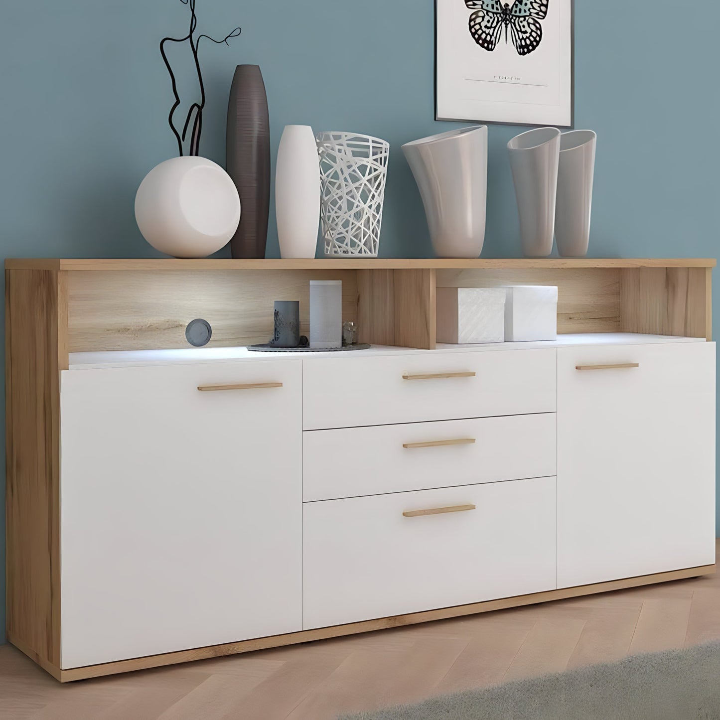 Wooden sideboard with white doors and drawers, decorated with vases and decor items against a blue wall.