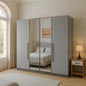 Gray wardrobe with mirror doors in a bedroom setting with a lamp and bed visible.