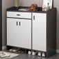 White shoe cabinet with black top and sides, shoes underneath, on a gray floor.
