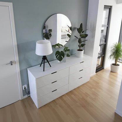 White dresser with a lamp, mirror, and plant in a room.