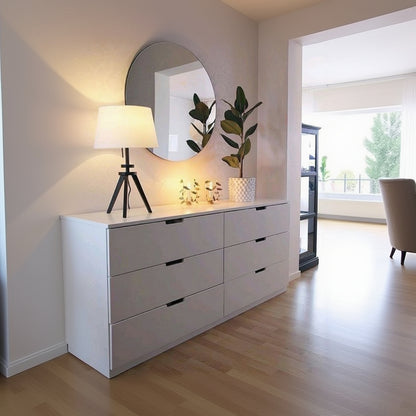 White dresser with round mirror, lamp, and plants in a room.