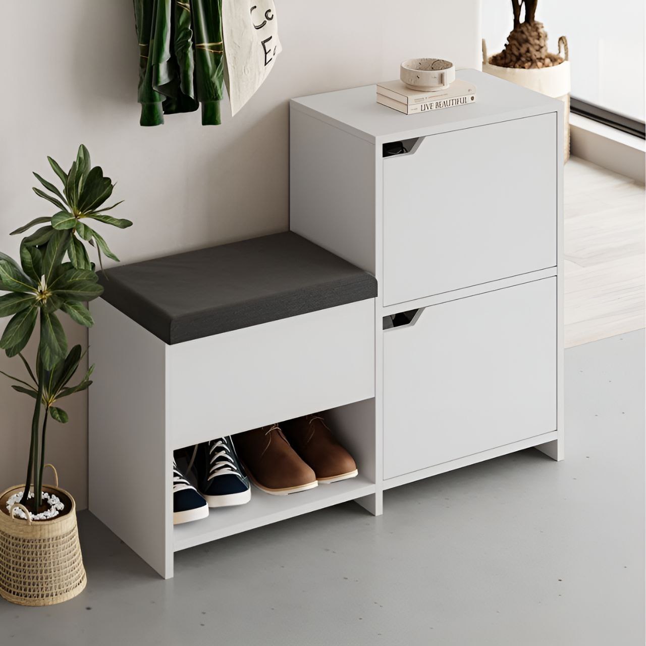 White shoe storage bench with gray cushion and two drawers, featuring shoes and a plant in a minimalistic setting.