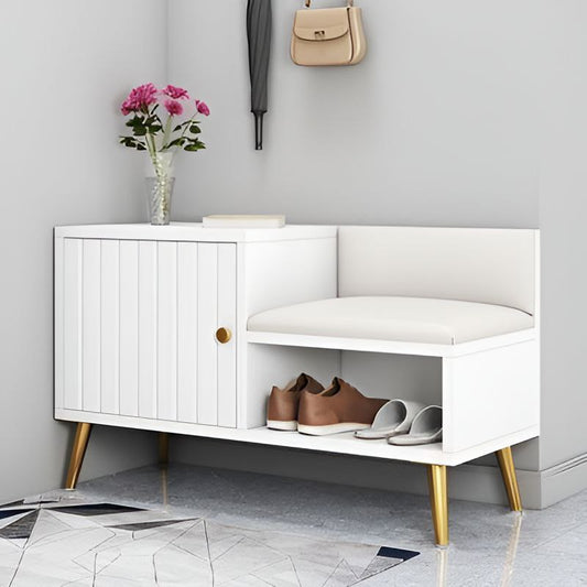White shoe cabinet with gold legs, shoes, a vase of flowers, and a handbag on a light gray wall.