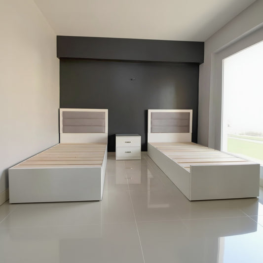 Two wooden beds with white frames against a dark wall.