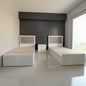 Two wooden beds with white frames against a dark wall.