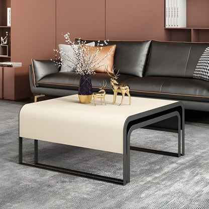 Modern living room with a black sofa, beige ottoman, and decorative items.